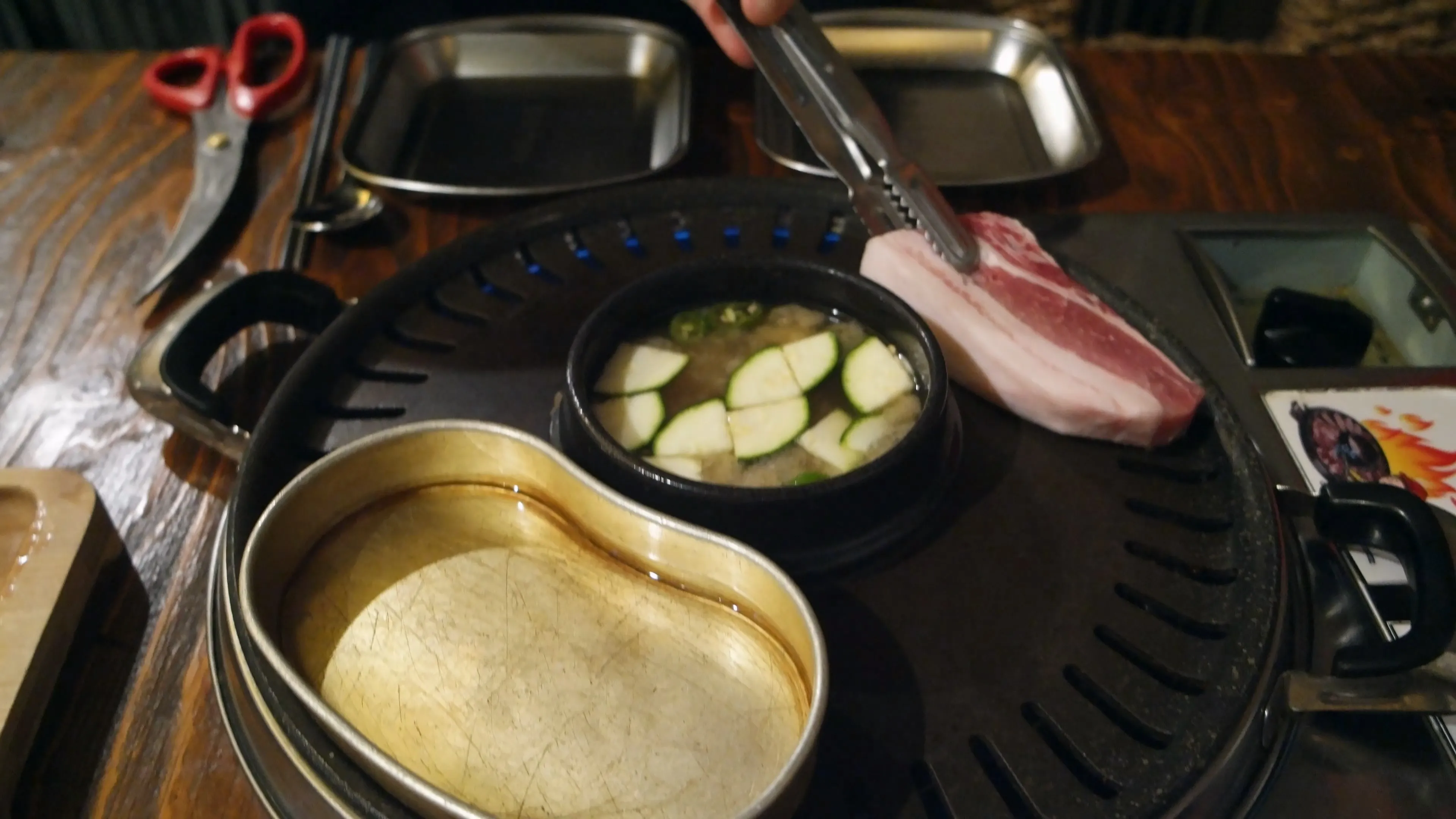 집게로 두툼한 생삼겹살을 불판 위에 올리는 장면